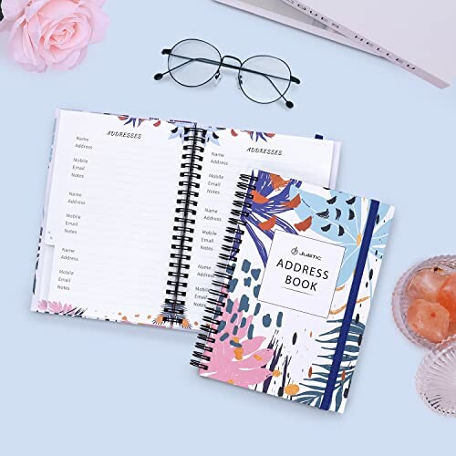Open address book with floral design next to glasses and flowers.