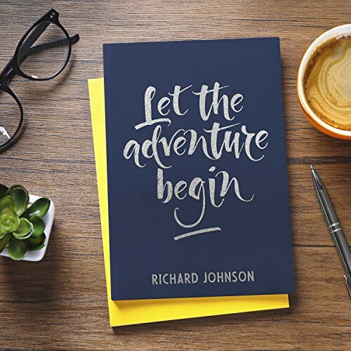 Notebook with 'Let the adventure begin' on a wooden table with coffee, glasses, and a pen.